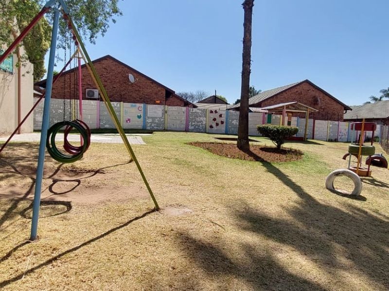 A communal garden area featuring a lawn, perimeter fencing, and basic playground equipment within an apartment complex setting.