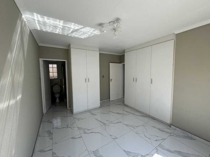 A bright, empty bedroom featuring modern marble-look floor tiles, ample built-in cupboard storage, and an en-suite bathroom access.