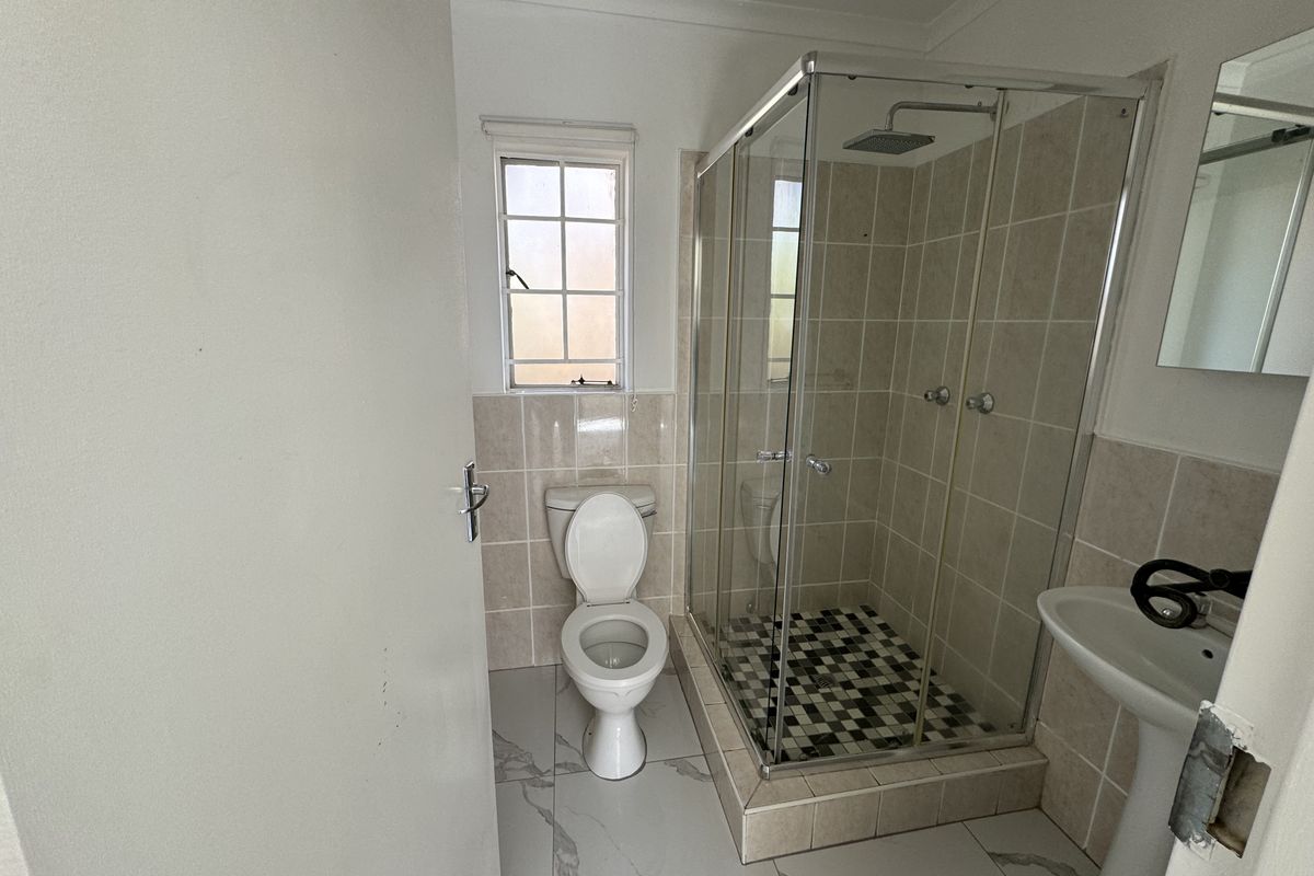 A clean, modern bathroom featuring a glass-enclosed shower with a rain shower head, pedestal basin, and neutral wall and floor tiling.
