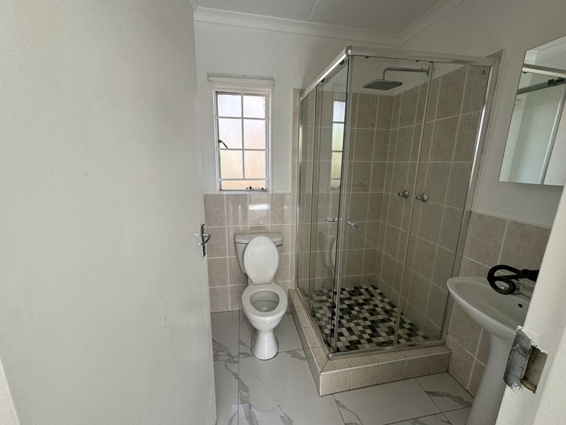 A clean, modern bathroom featuring a glass-enclosed shower with a rain shower head, pedestal basin, and neutral wall and floor tiling.