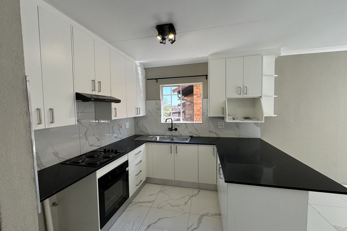 Modern kitchen featuring white cabinetry, black granite countertops, marble-look tile flooring, and integrated appliances including an electric hob and oven.