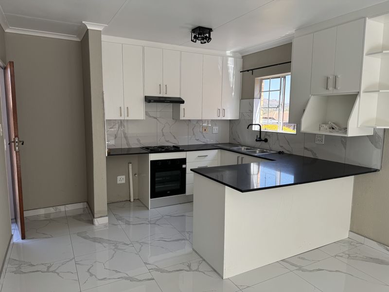 Modern kitchen featuring white cabinetry, black granite countertops, marble-look tiled backsplash, built-in oven, hob, and extractor fan with sleek porcelain floor tiles.
