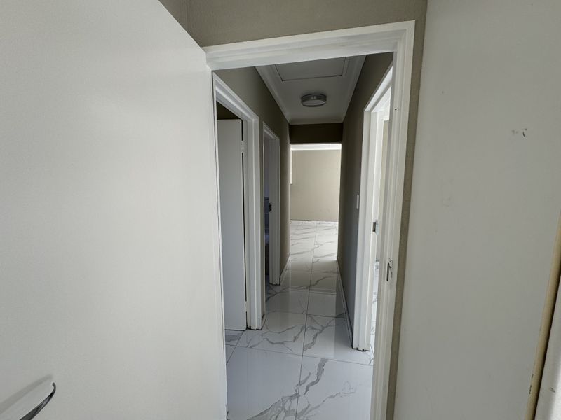 A bright, empty hallway featuring modern marble-look floor tiles and access to multiple rooms, providing a clean and neutral transition space.