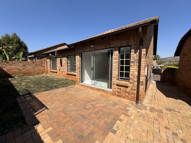 Rear view of a brick townhouse featuring a paved patio area, sliding glass doors, and a private garden space.
