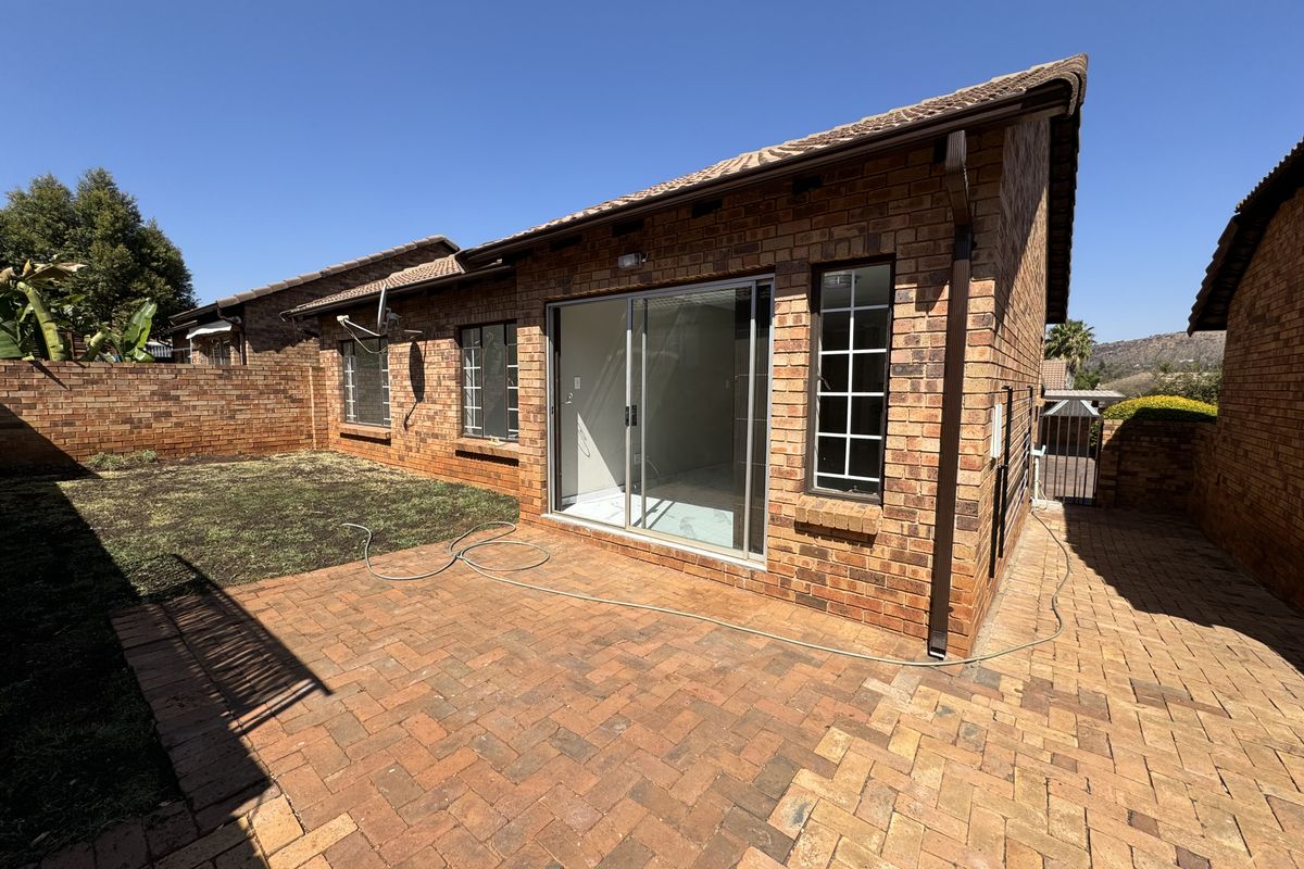 Rear view of a brick townhouse featuring a paved patio area, sliding glass doors, and a private garden space.