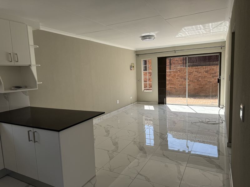 Bright open-plan living and kitchen area featuring modern marble-look floor tiles, white cabinetry with dark countertops, and direct access to a rear patio.