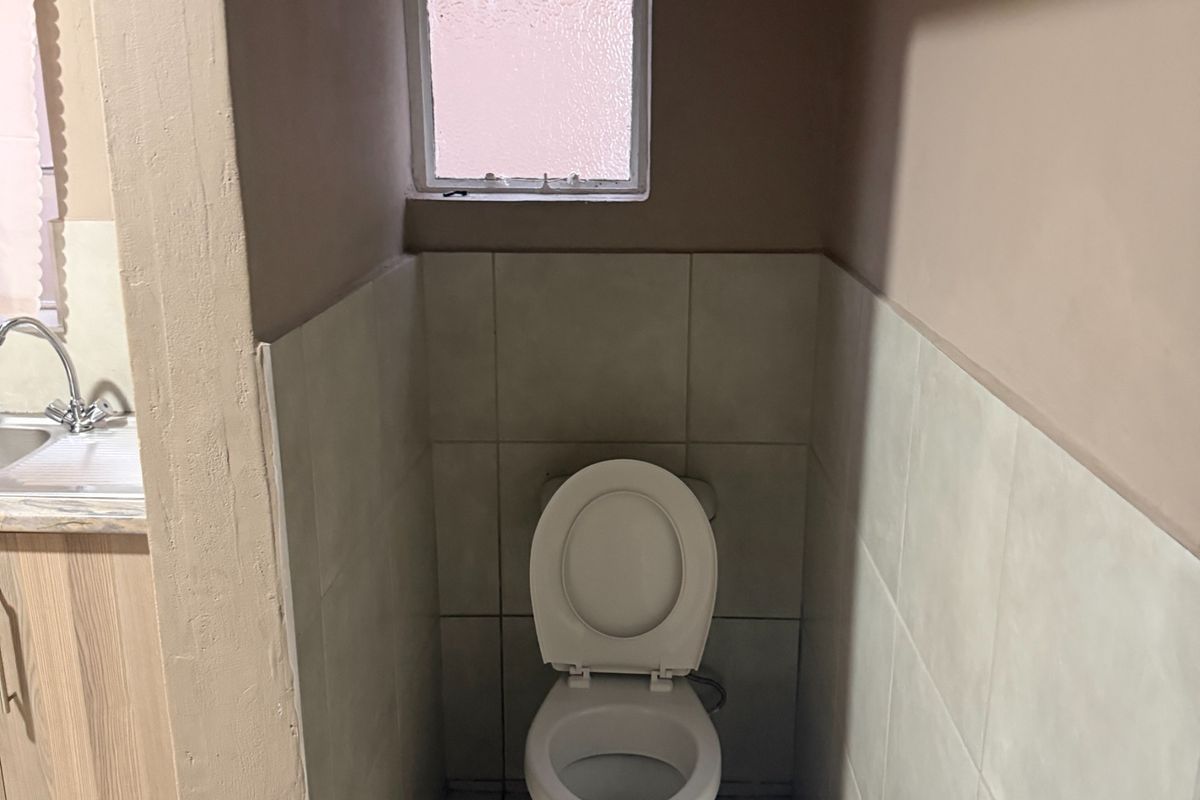 A functional bathroom featuring a toilet, wall-mounted basin, and a secondary vanity area with a sink, finished with neutral wall tiles.