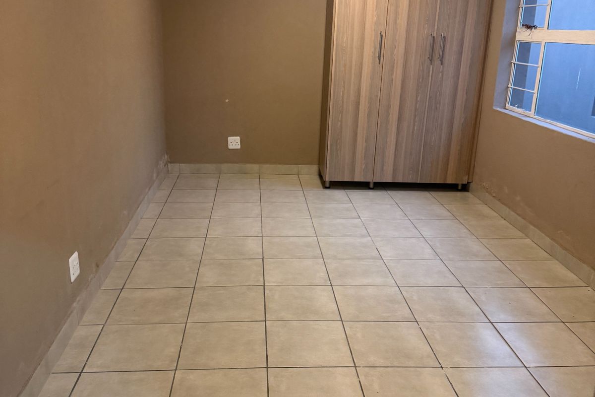 A vacant bedroom featuring tiled flooring, built-in wooden cupboards, and a window with security bars.