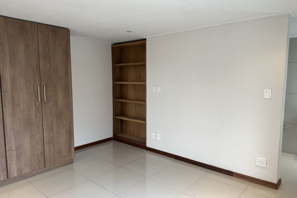 A bright bedroom featuring built-in wooden cabinetry, integrated shelving, tiled flooring, and neutral wall finishes.