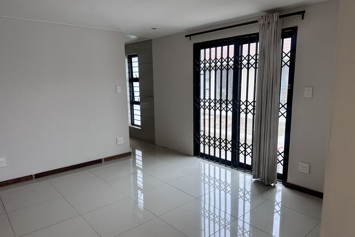 A bright, empty living area featuring large format floor tiles, recessed downlighting, and a secure sliding door with an integrated security gate.