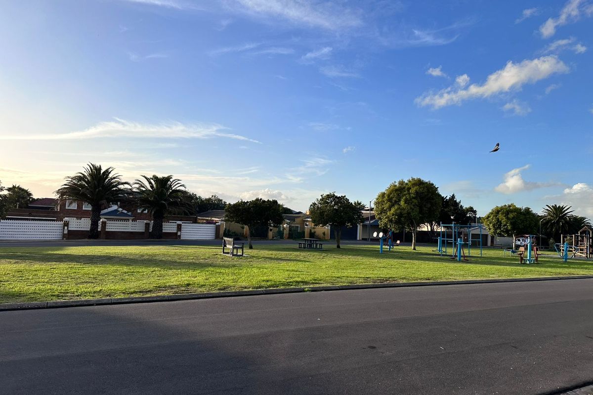 A view of a public park area with green lawns, mature trees, and outdoor exercise equipment located near residential properties.