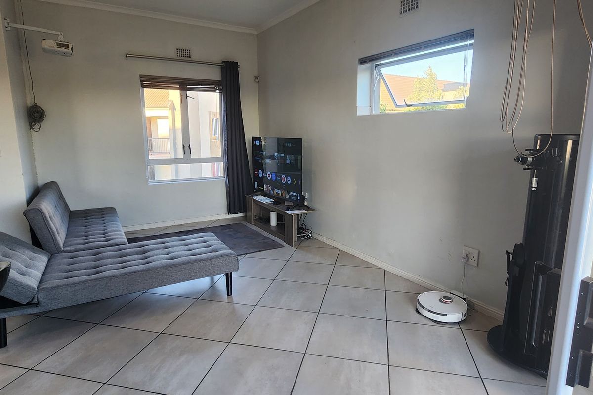 A living room featuring tiled flooring, a large window, and a high-level horizontal window, providing natural light and a functional layout.