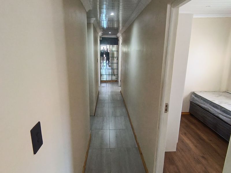 A clean, tiled hallway featuring a glossy panelled ceiling, providing access to adjacent rooms including a bedroom with wood-look flooring.