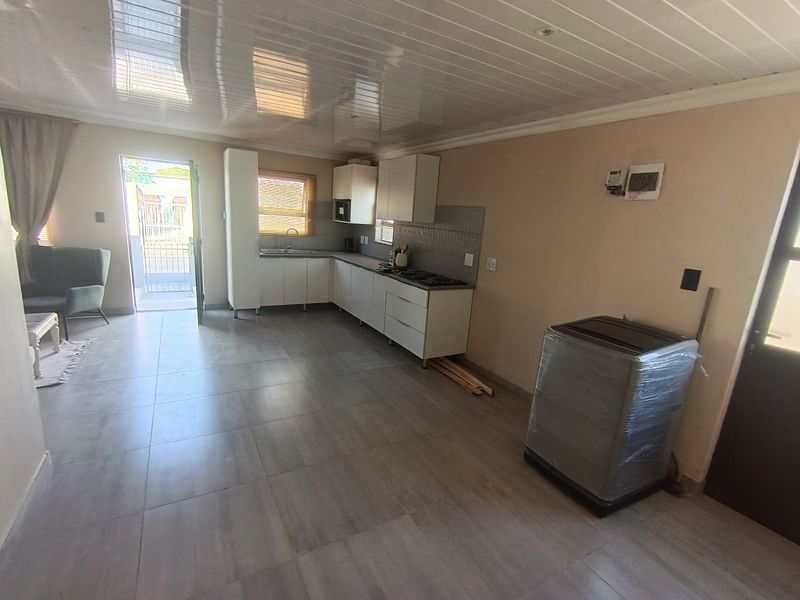 Open plan kitchen and living area featuring modern tiled flooring, white cabinetry, a built-in hob, and a PVC ceiling with direct access to the exterior.