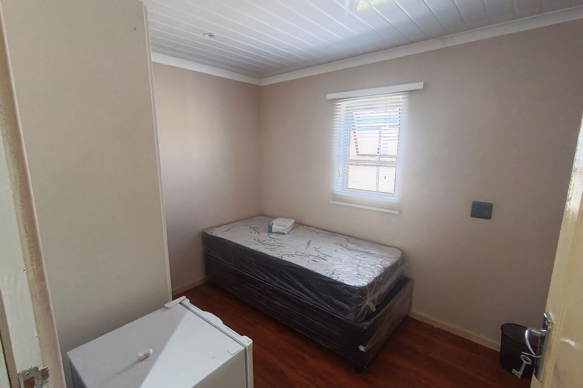 A compact bedroom featuring laminate flooring, a tongue and groove ceiling, and a window fitted with venetian blinds.