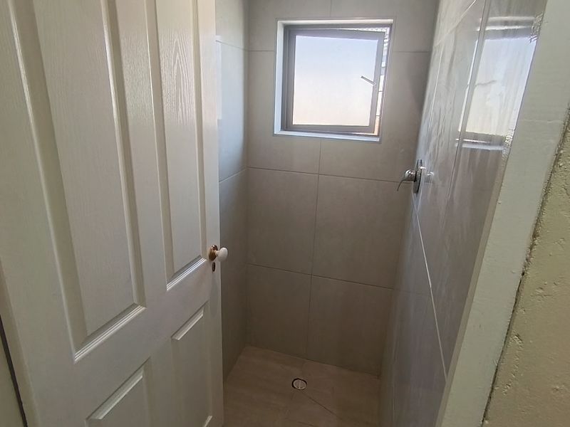 A compact, tiled shower enclosure featuring a wall-mounted shower head, mixer, and a small window for natural light.