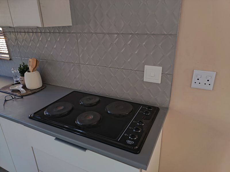 A clean kitchen workspace featuring a built-in electric hob, grey textured tiled splashback, and modern laminate countertops with integrated cabinetry.