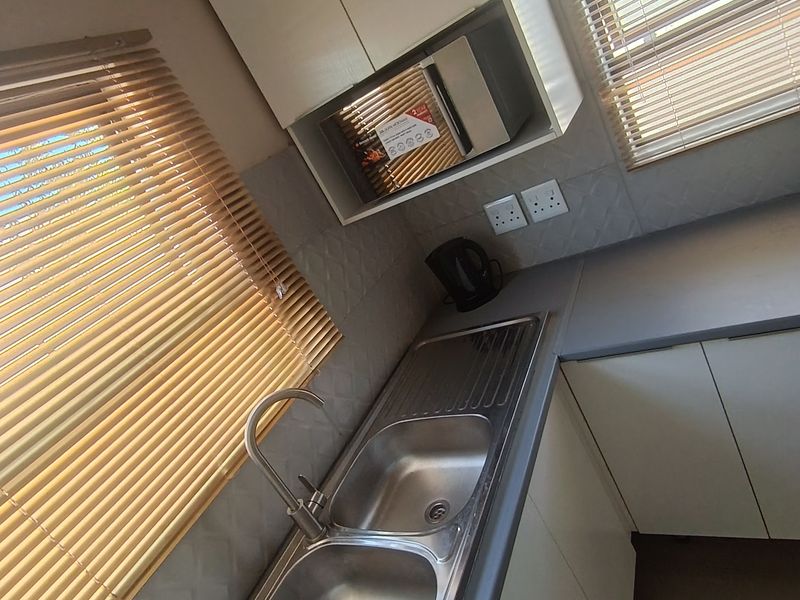 A clean and functional kitchen area featuring a double bowl stainless steel sink, built-in microwave, and ample cabinetry with a modern tiled backsplash.