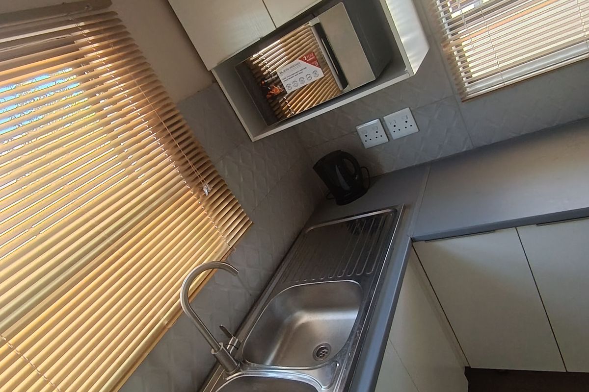 A clean and functional kitchen area featuring a double bowl stainless steel sink, built-in microwave, and ample cabinetry with a modern tiled backsplash.