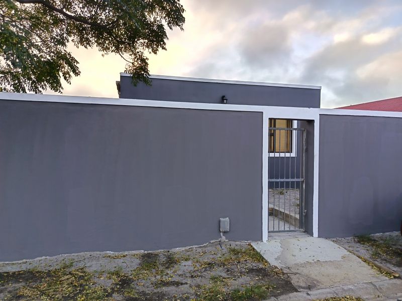 A view of the property's front boundary wall featuring a secure metal pedestrian gate and exterior lighting.