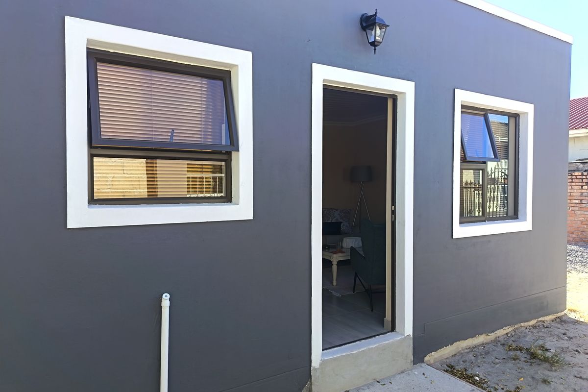 A view of the rear exterior wall featuring dark grey painted finish, white window frames, and a central doorway leading into the home.