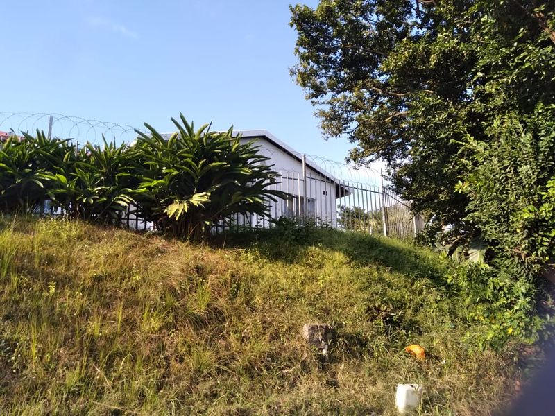 View of the rear exterior of the cottage, featuring a sloped garden area and secure metal perimeter fencing with razor wire.