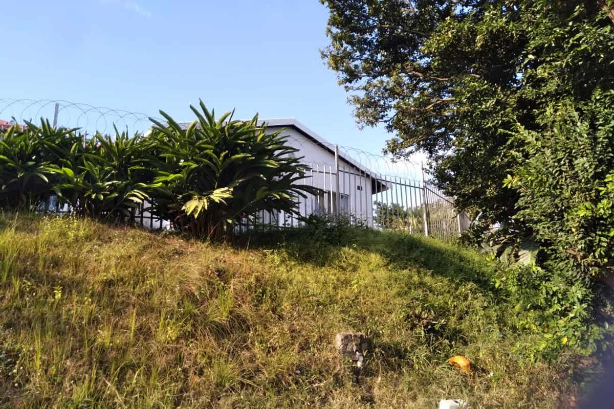 View of the rear exterior of the cottage, featuring a sloped garden area and secure metal perimeter fencing with razor wire.
