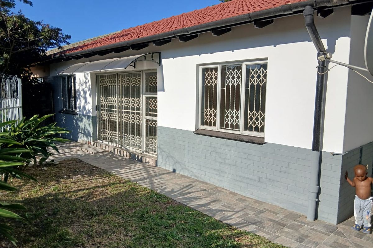 Rear view of the cottage featuring a tiled roof, painted brick exterior, security gates, and a paved walkway along the building perimeter.