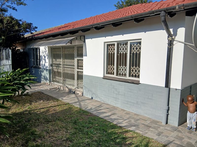Rear view of the cottage featuring a tiled roof, painted brick exterior, security gates, and a paved walkway along the building perimeter.