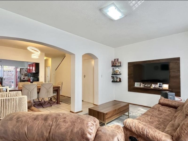 Spacious open-plan living and dining area featuring tiled flooring, arched architectural details, and a modern built-in television wall panel.