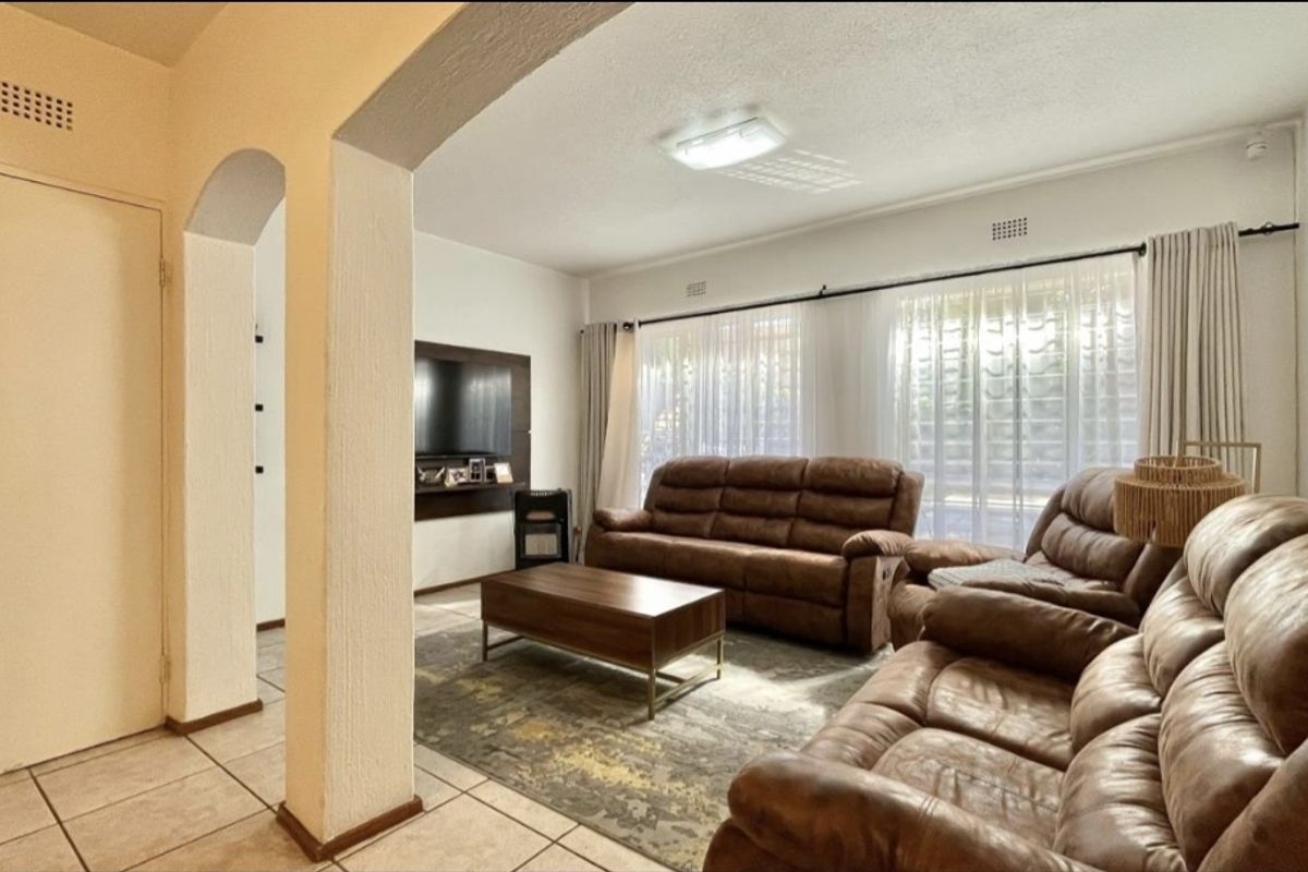 A spacious living room featuring tiled flooring, an architectural archway, and large windows with curtain rails, providing a bright and functional living space.