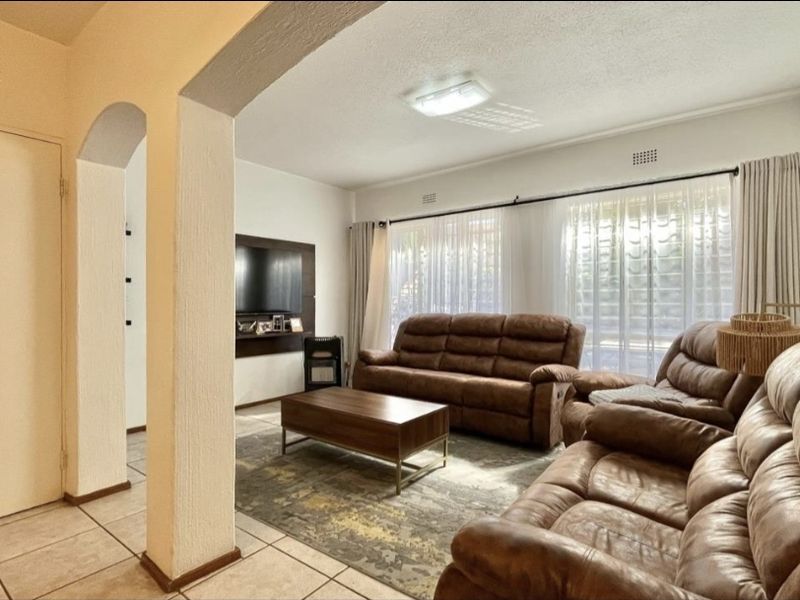 A spacious living room featuring tiled flooring, an architectural archway, and large windows with curtain rails, providing a bright and functional living space.