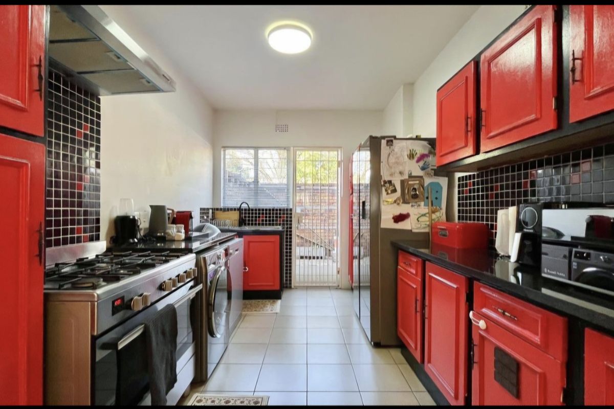 A functional kitchen featuring red cabinetry, a gas stove with extractor fan, tiled backsplash, and direct access to an outdoor area via a security gate.