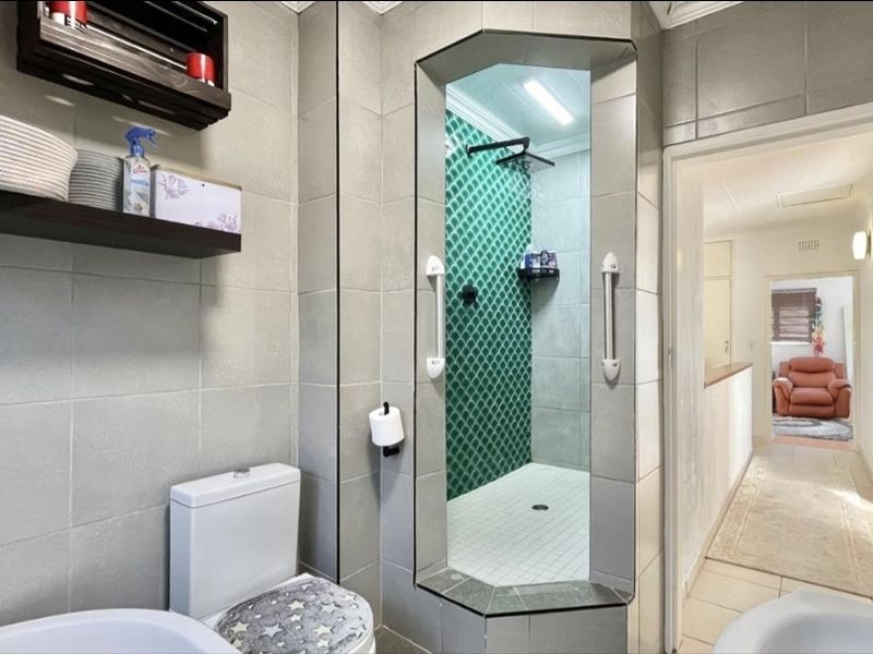 Modern bathroom featuring a walk-in shower with green decorative tiling, neutral wall tiles, and functional grab rails.
