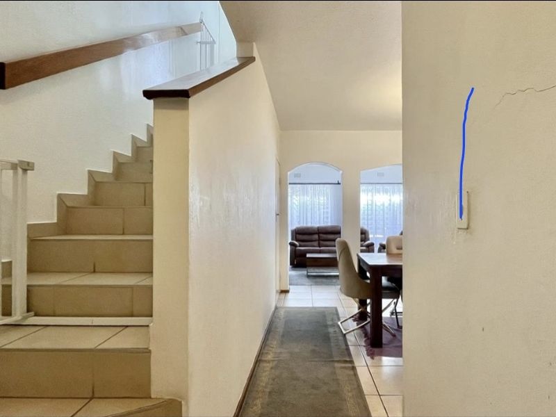 A hallway featuring a tiled staircase with a wooden handrail and a metal safety gate, showing visible wall cracking requiring maintenance.