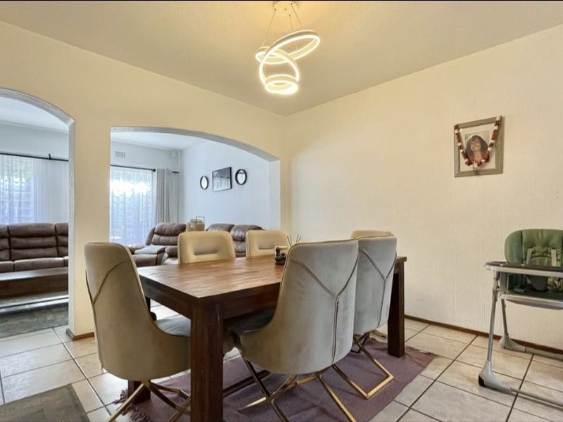 A bright dining area featuring tiled flooring and arched architectural openings leading into the adjacent living space, illuminated by a contemporary pendant light.