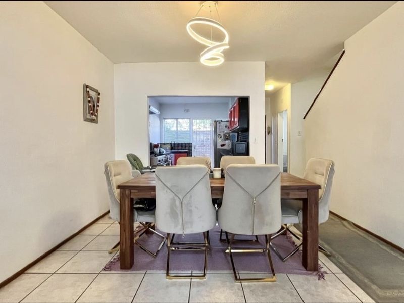Open plan dining area featuring tiled flooring and a modern pendant light fixture, with a view through to the kitchen area.