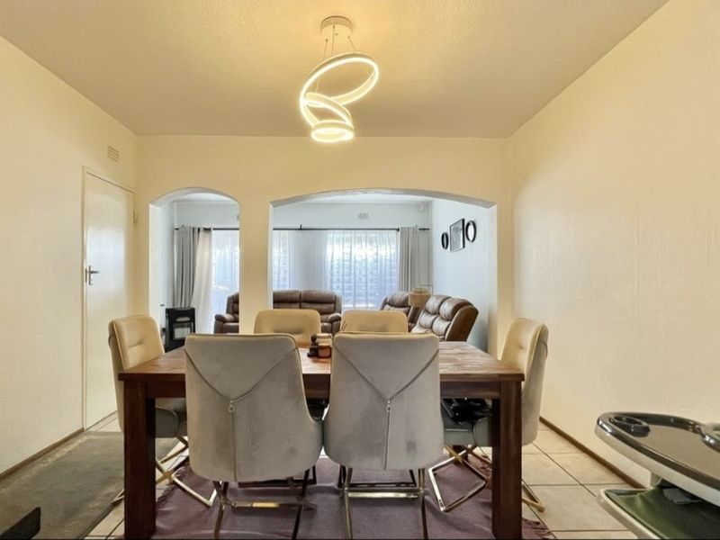 An open-plan dining and living area featuring tiled flooring, a central archway, and a modern pendant light fixture.