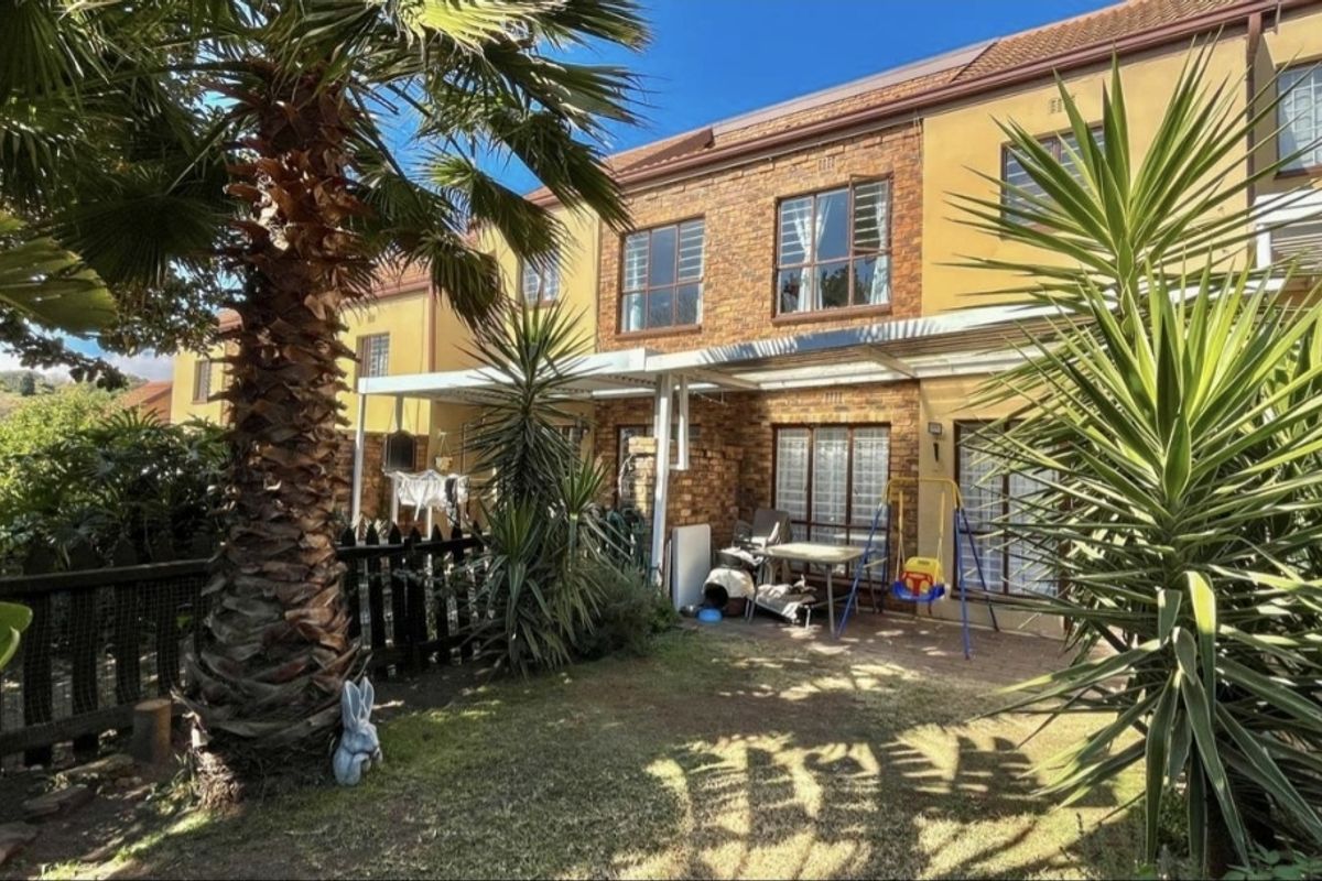 Rear view of the apartment featuring a brick facade, a paved patio area with a covered structure, and a private garden space.