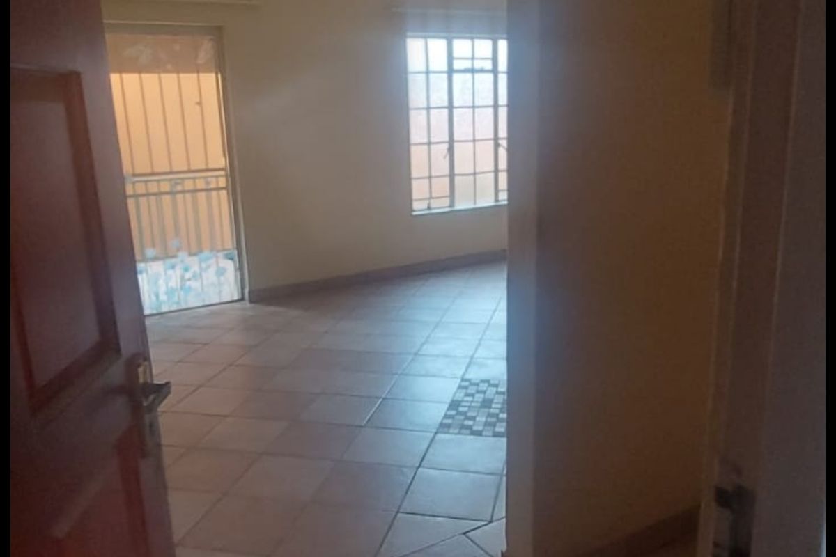 An empty living area featuring tiled flooring, natural light, and access to a balcony with security gate.
