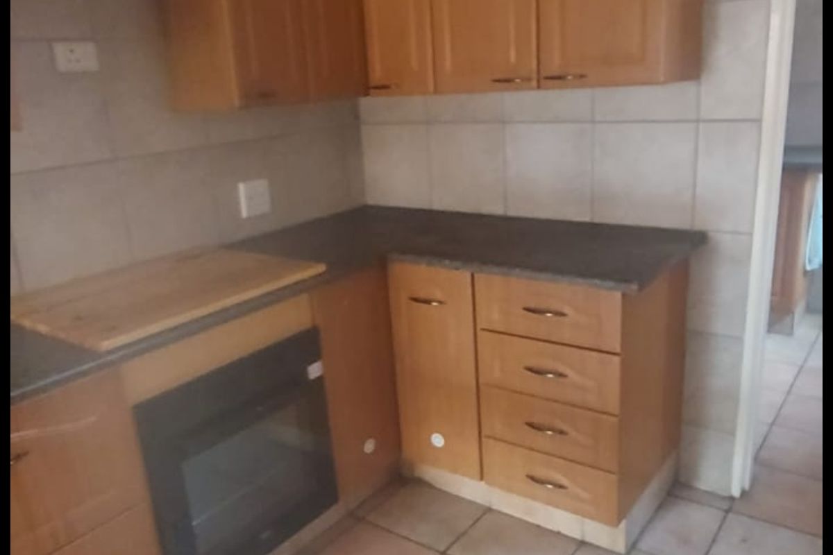 A dated kitchen featuring wooden cabinetry, laminate countertops, and a built-in oven, finished with ceramic wall and floor tiles.