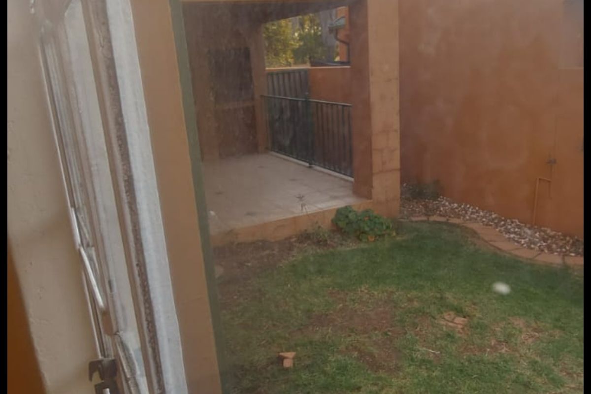 A view of the rear exterior of the apartment, featuring a small lawn, a covered patio area with metal railings, and a satellite dish.
