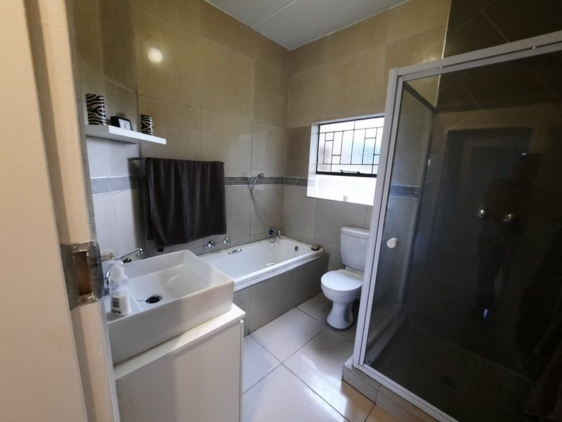 A functional bathroom featuring a built-in bathtub, separate shower enclosure, basin, and toilet with neutral wall and floor tiling.