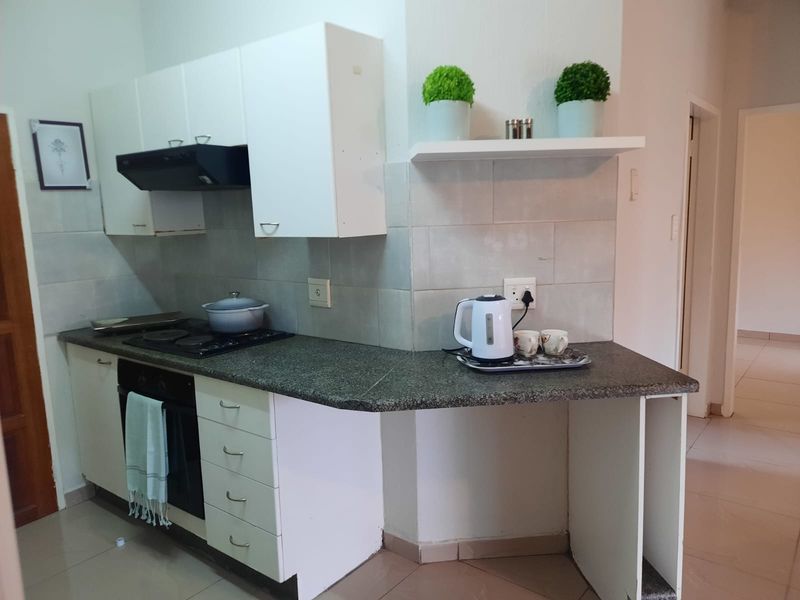 Compact kitchen featuring built-in cabinetry, granite countertops, an electric hob, oven, and extractor fan with a tiled backsplash.