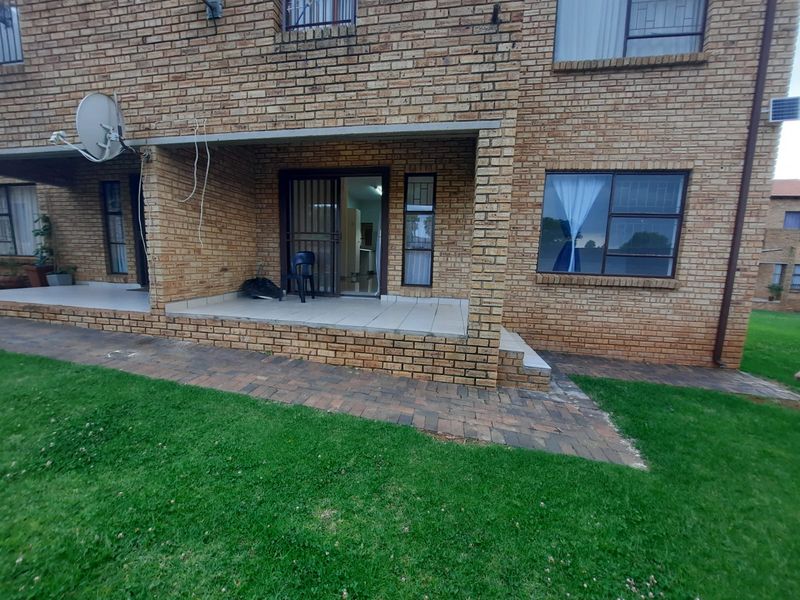 Rear view of a face brick apartment building featuring a covered tiled patio, sliding glass doors, and a paved walkway leading to the lawn.