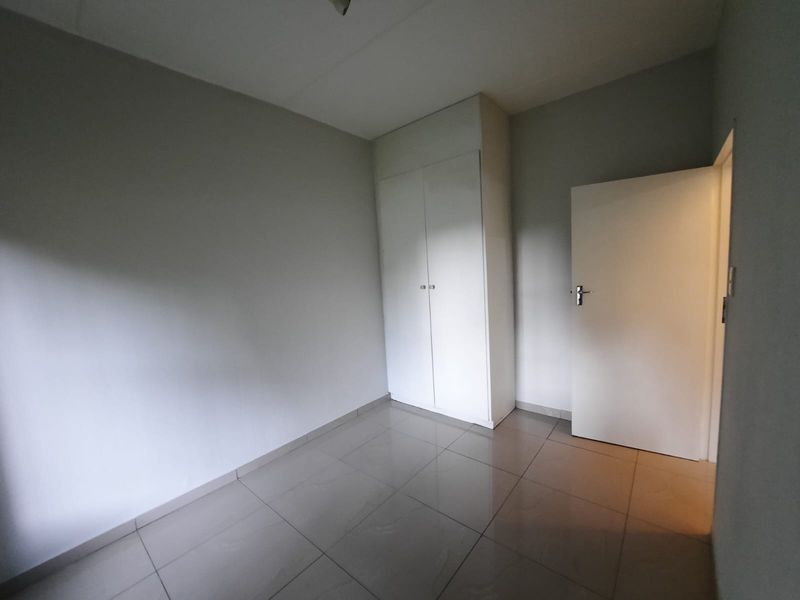 An empty bedroom featuring neutral tiled flooring and a built-in white cupboard, offering a clean and versatile space.