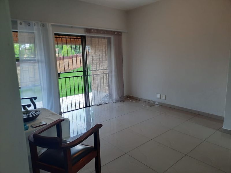 A bright, empty living room featuring large format floor tiles and a sliding glass door providing direct access to the outdoor patio area.