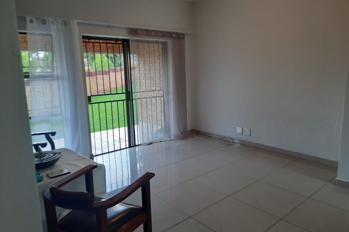 A bright, empty living room featuring large format floor tiles and a sliding glass door providing direct access to the outdoor patio area.