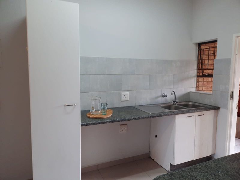 A functional kitchen area featuring granite countertops, a stainless steel double sink, tiled backsplash, and built-in cabinetry with security bars on the window.