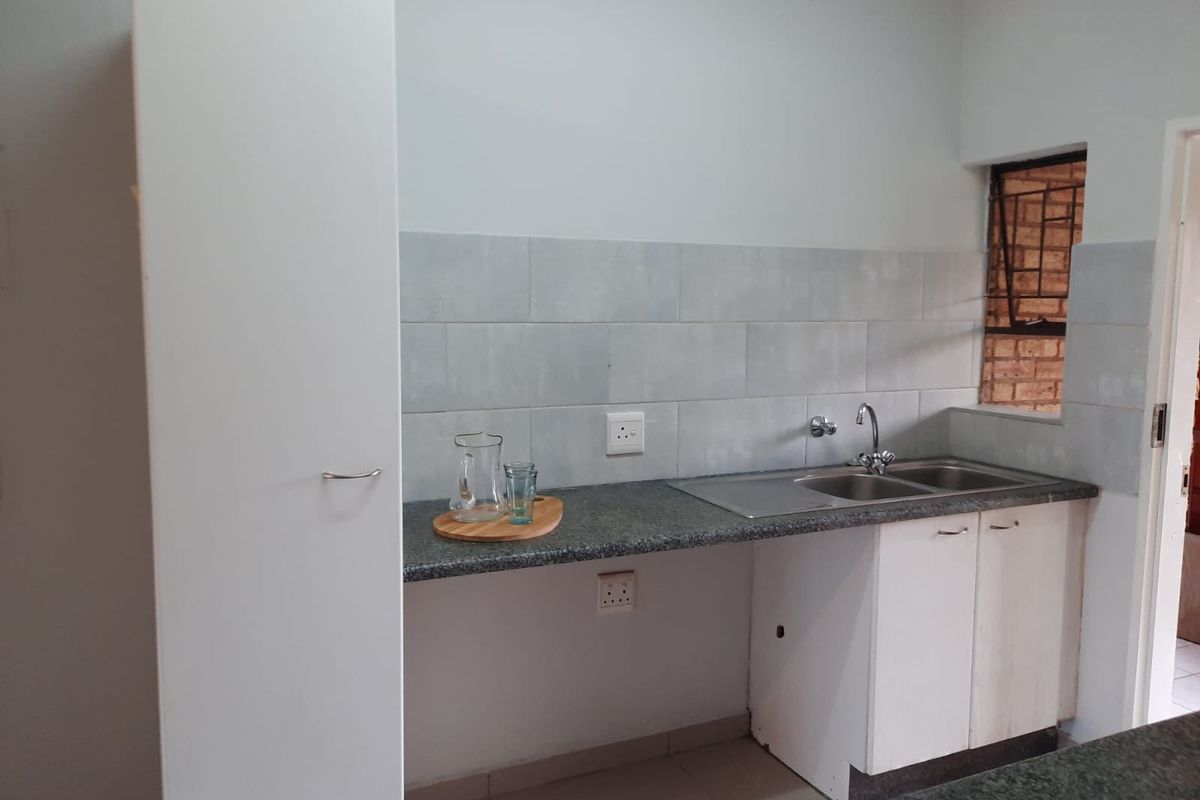 A functional kitchen area featuring granite countertops, a stainless steel double sink, tiled backsplash, and built-in cabinetry with security bars on the window.